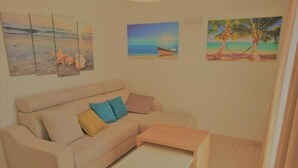A living room with a beige sofa, a coffee table, and three paintings on the wall.