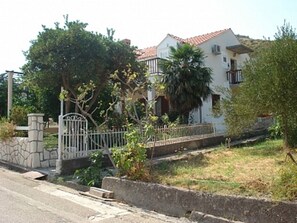 A two-story house with a tiled roof, a stone wall, and a metal gate. - Sea Apartments Slano (Dubrovacko Primorje)