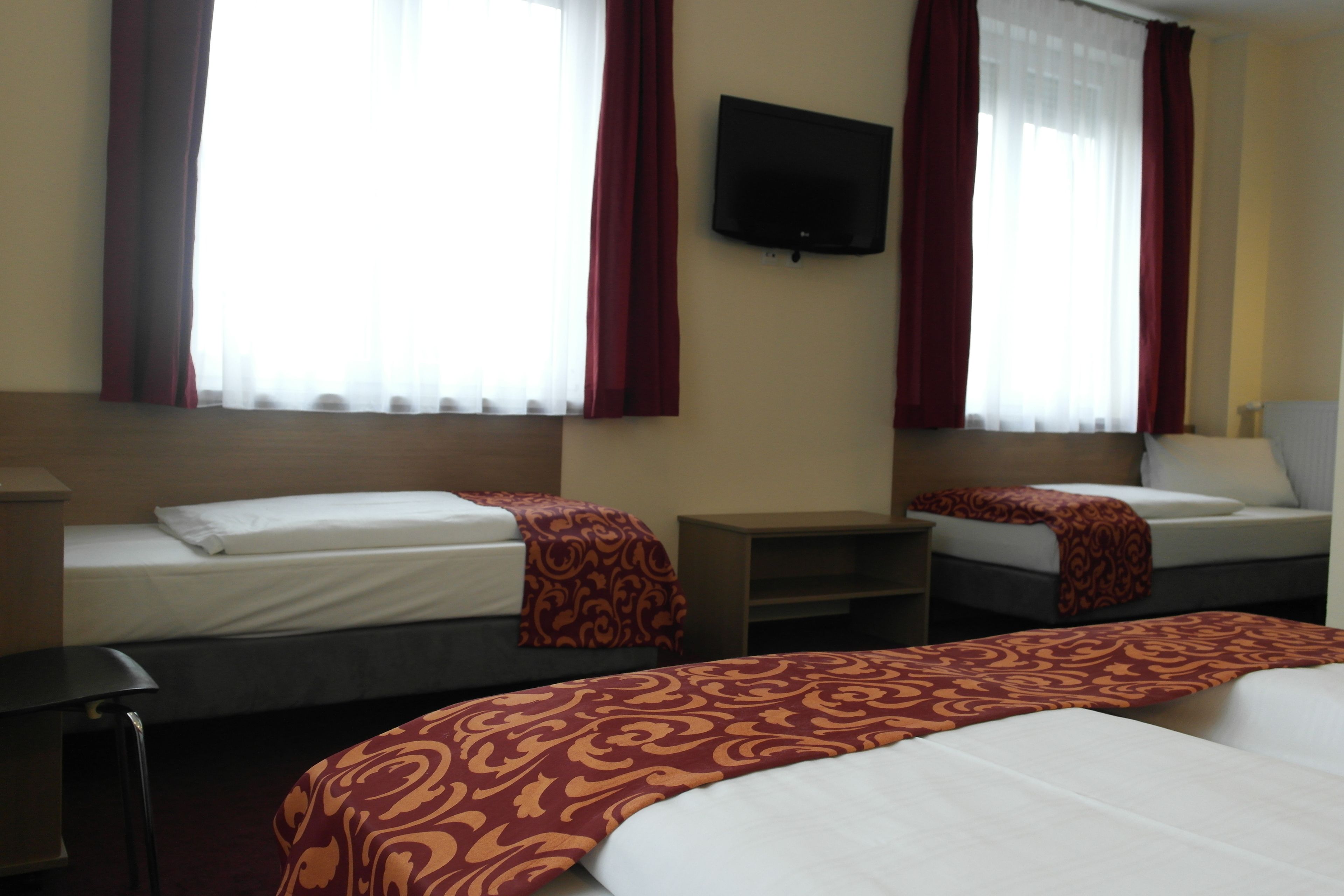 Une chambre d’hôtel avec deux lits, un téléviseur fixé au mur et une fenêtre avec des rideaux.