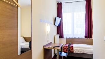 Quarto de hotel com uma cama, uma mesa, uma cadeira, uma televisão e um espelho.