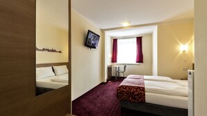 A hotel room with a bed, a desk, a chair, a TV, and a window with curtains. - Dream Inn Hotel Regensburg (Tegernheim)