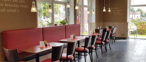 A restaurant interior with red booths and wooden tables, large windows, and hanging pendant lights.