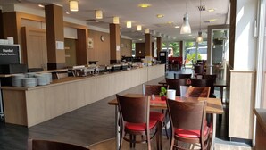 A modern cafe with a long counter, multiple tables, and chairs. - Dream Inn Hotel Regensburg (Tegernheim)