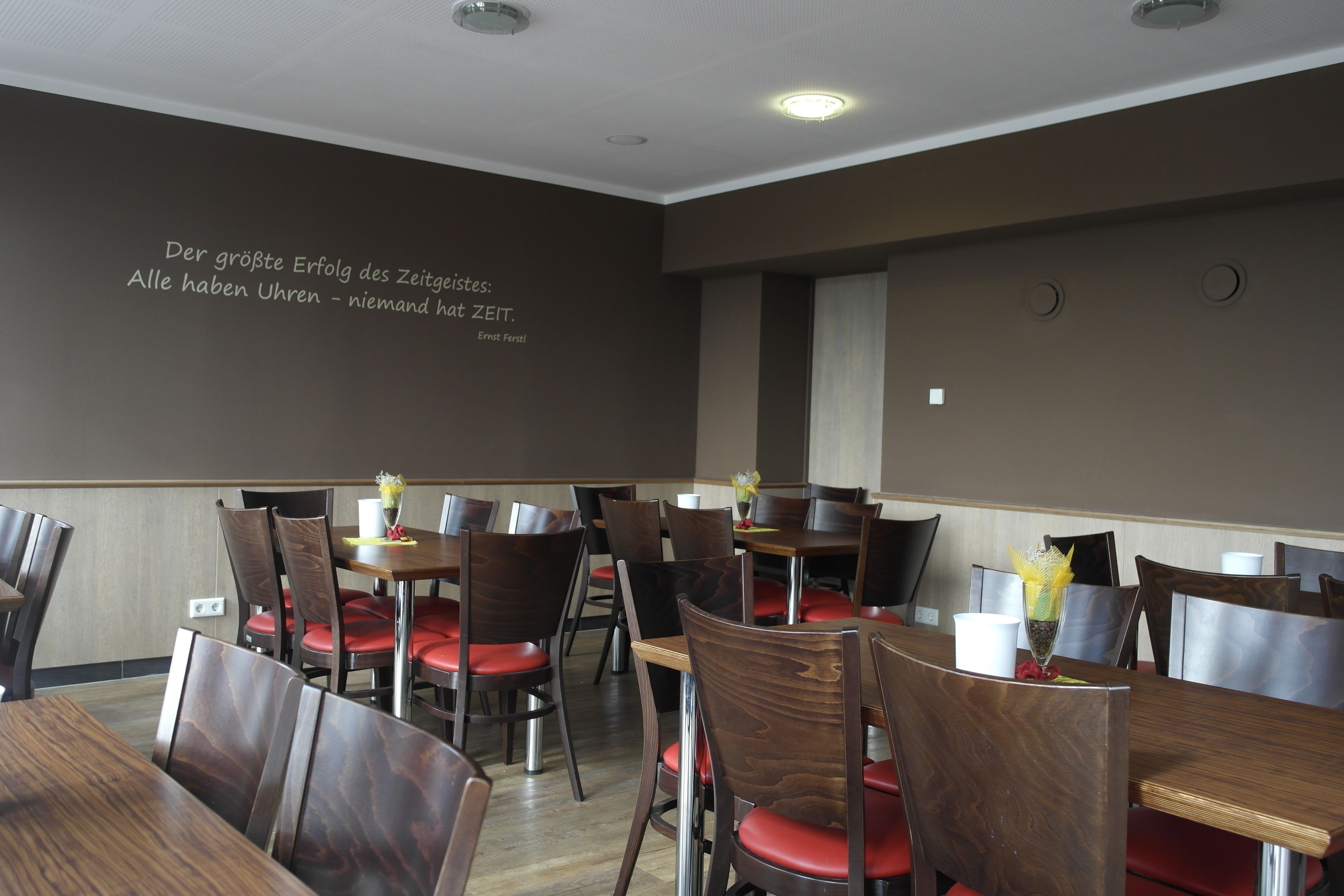 A dining area with wooden tables and chairs, a wall with a quote, and a clock on the wall.