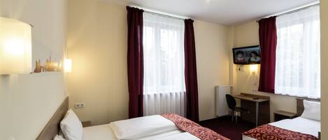 A hotel room with two beds, a desk, a chair, and a TV.