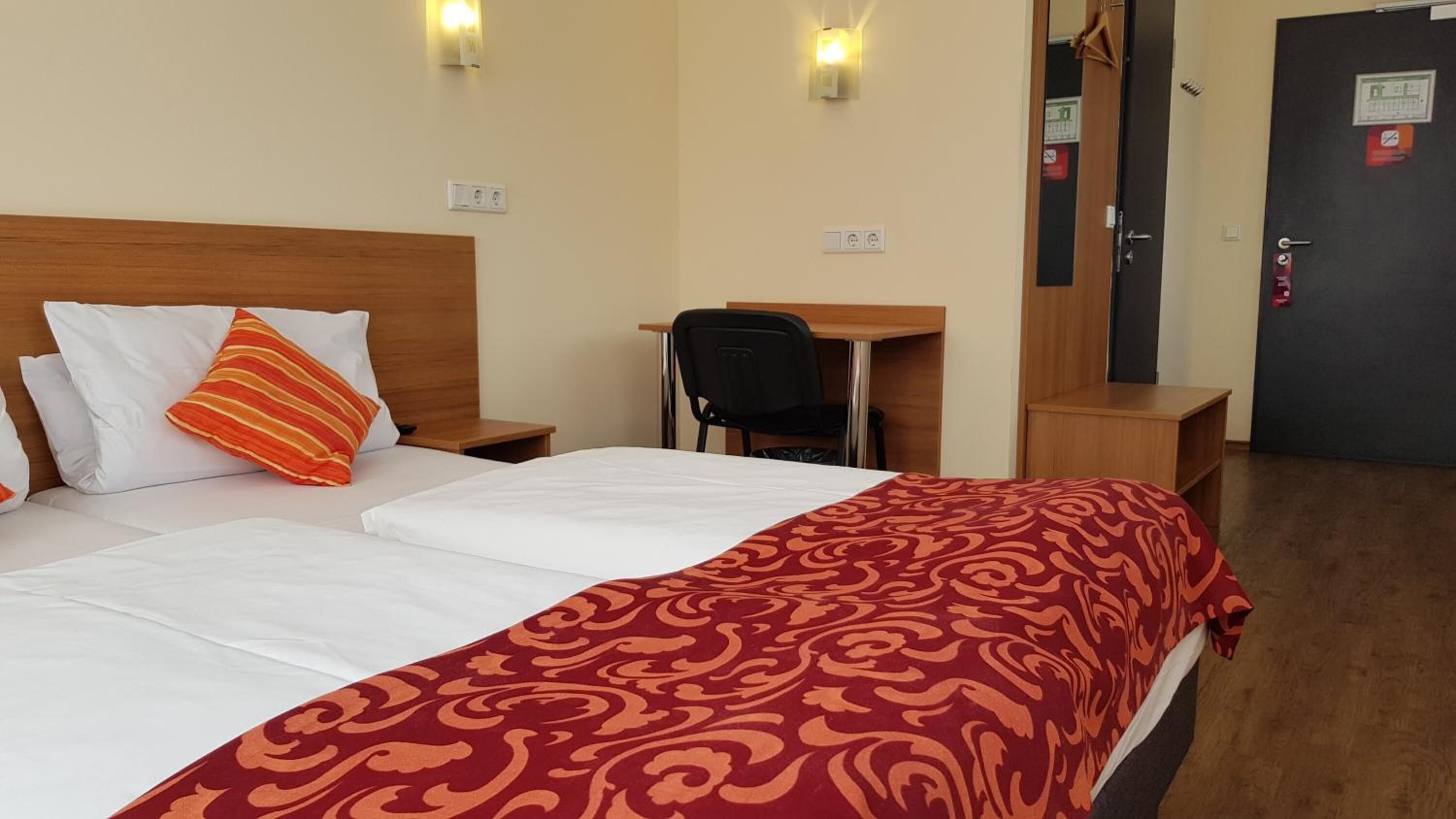 Habitación de hotel con cama, escritorio y silla. Dos lámparas de pared sobre la cama.