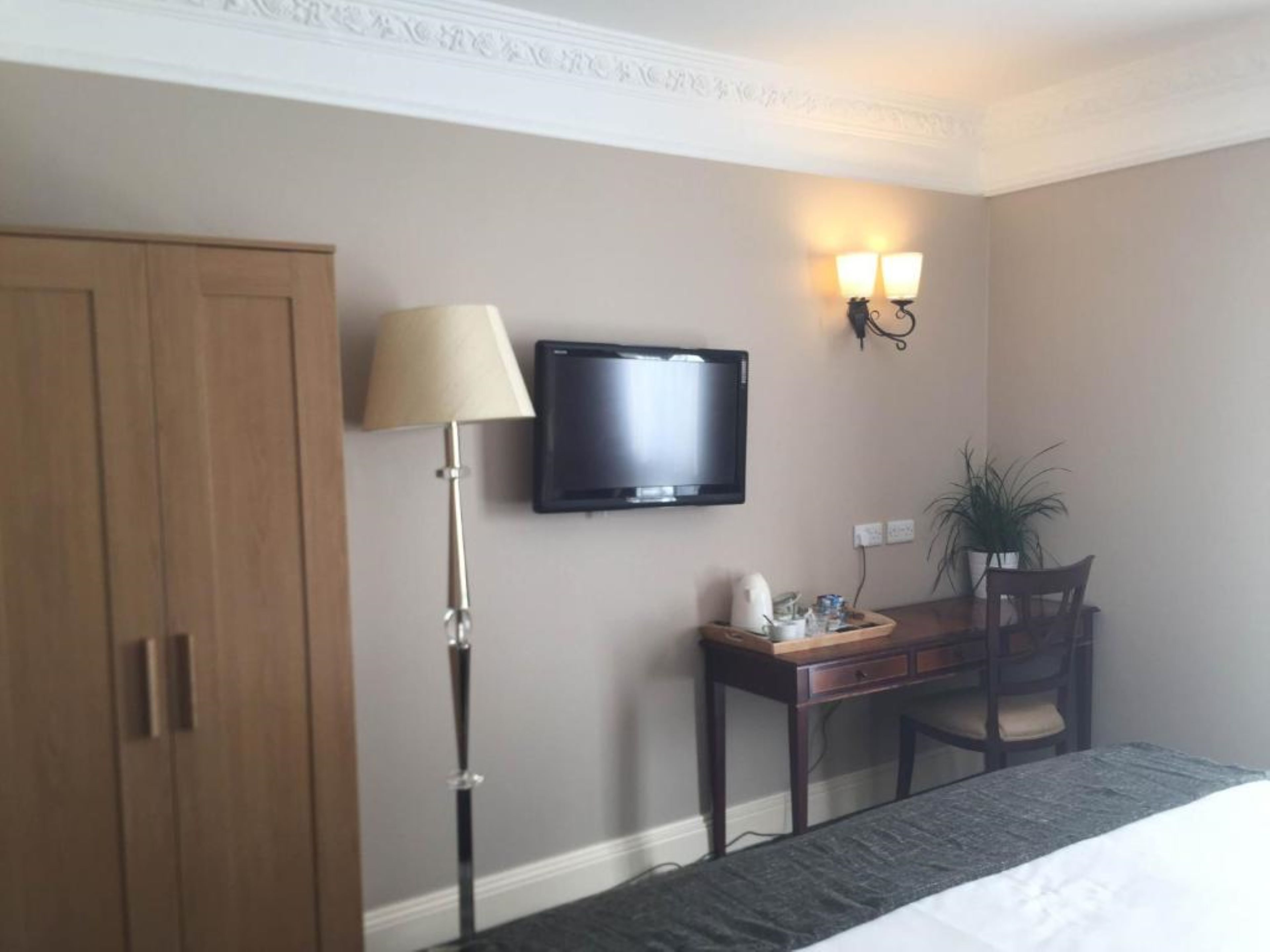 Una habitación de hotel con cama, escritorio con lámpara, televisor y armario.