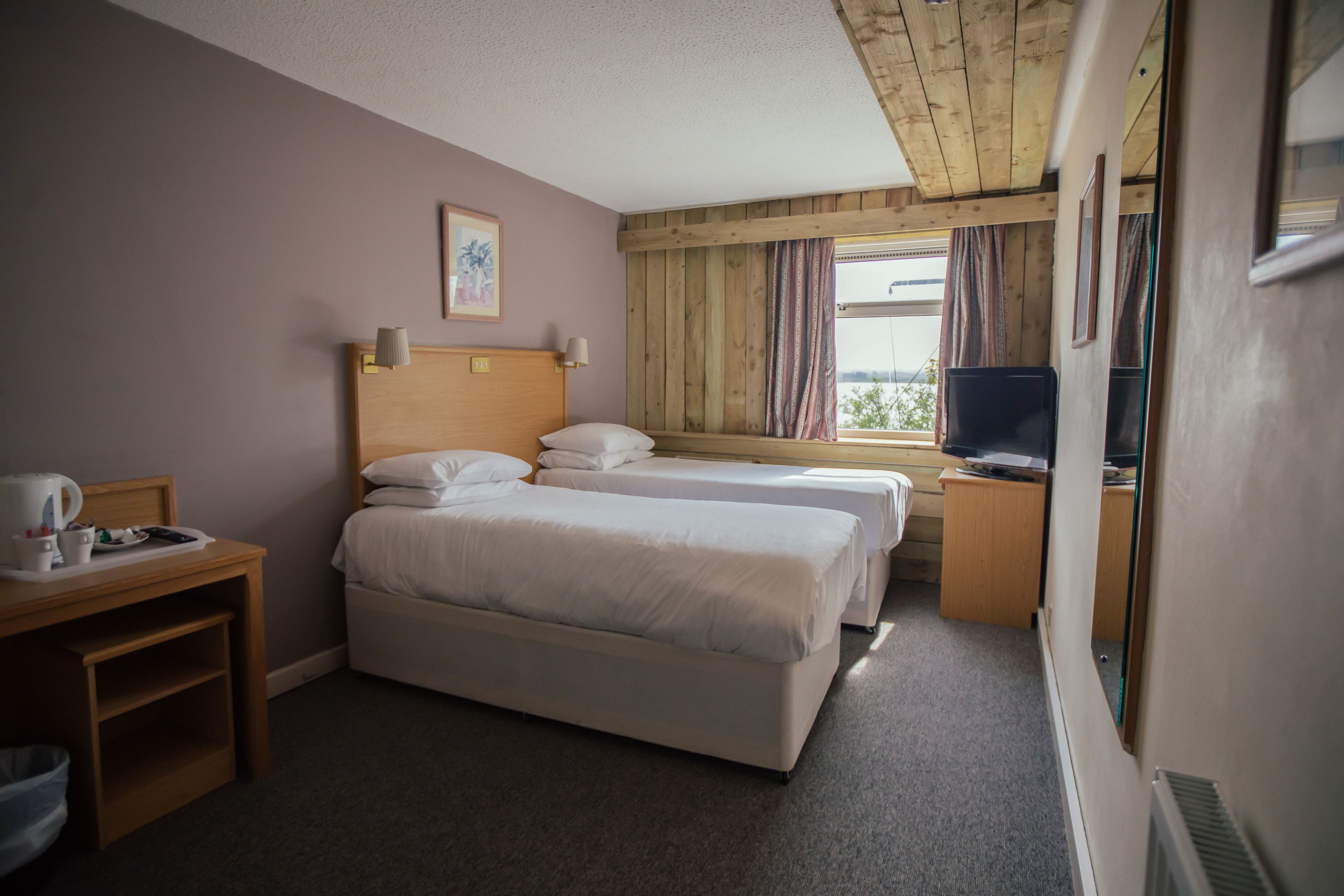 A hotel room with two beds, a desk with a lamp, a television, and a window with curtains.