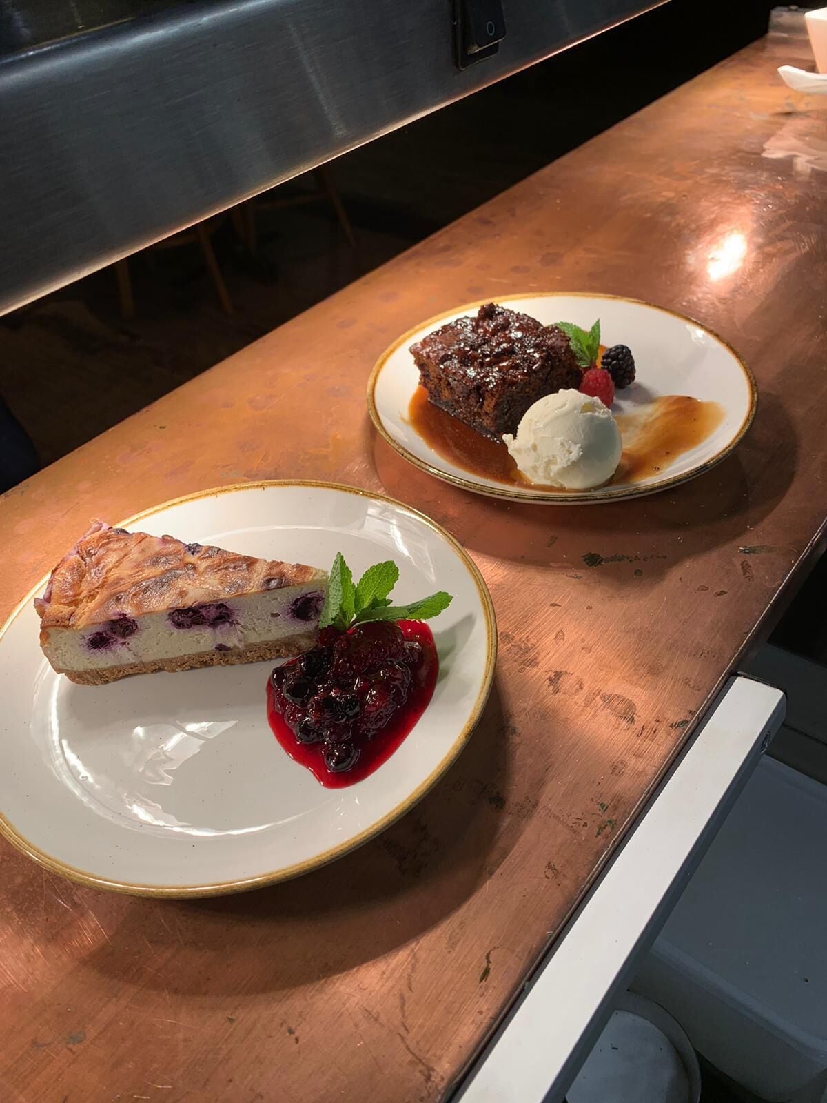 Een dessertbord met een plakje taart en een bolletje ijs, en een ander bord met een stukje cake en bessen.