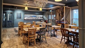Un restaurante con mesas y sillas de madera, una zona de bar y un candelabro.