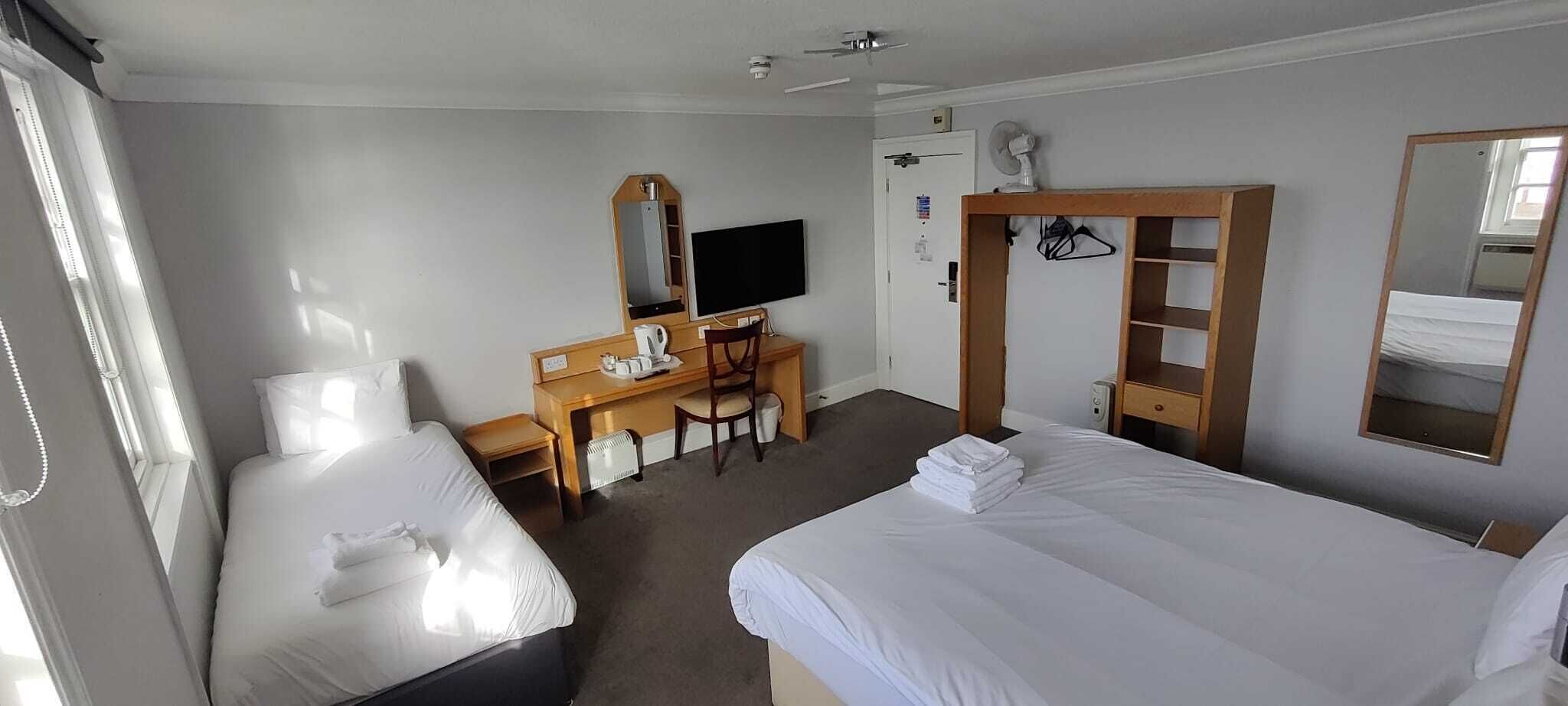 A hotel room with two beds, a desk with a chair, a television, a wardrobe, and a mirror.