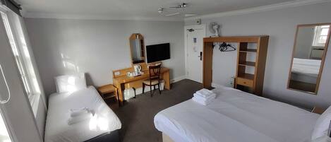 A hotel room with two beds, a desk with a chair, a television, a wardrobe, and a mirror.