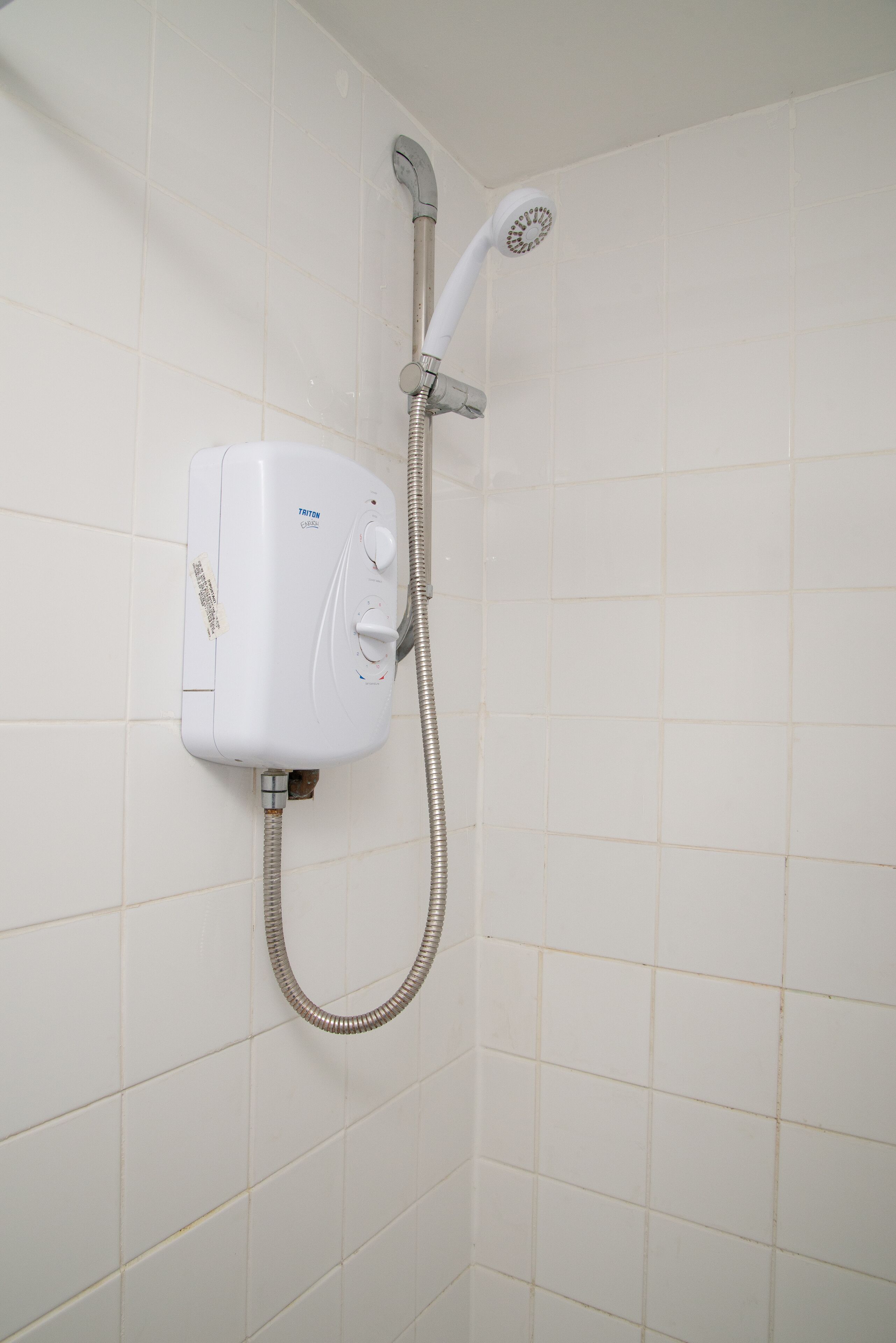 A wall-mounted shower unit with a handheld showerhead and a flexible hose.