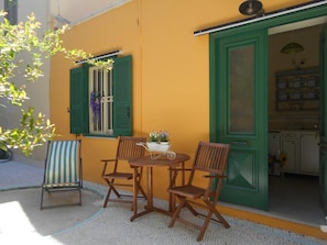 A small outdoor seating area with a round table and four wooden chairs, a striped chair, and a potted plant with flowers. - Florida Hotel (Rhodes)