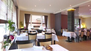 Un espace repas avec des tables préparées pour deux personnes, agrémenté de nappes blanches et de chaises foncées.