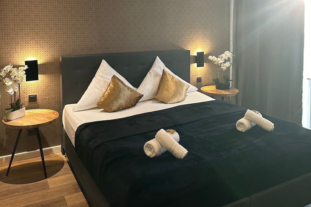 A modern hotel room with a large bed, two bedside tables, and a nightstand.