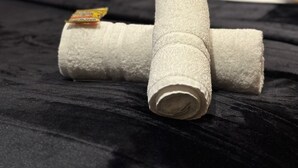 Un lit avec des serviettes enroulées et une table de chevet sur laquelle se trouvent une lampe et une petite plante.