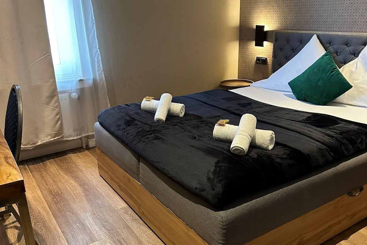 A neatly made bed with a dark headboard, a bedside table, and a wall-mounted light fixture.