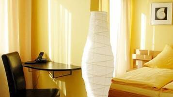 Una habitación de hotel con piso de madera, una cama con ropa de cama amarilla, un escritorio con silla y una lámpara de pie.