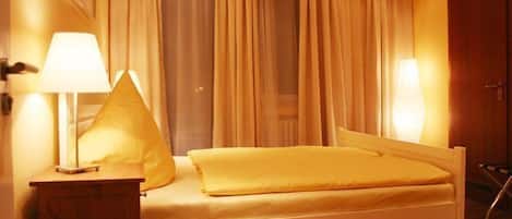 A bed with a white frame and a yellow bedspread, two bedside lamps, and a window with curtains.