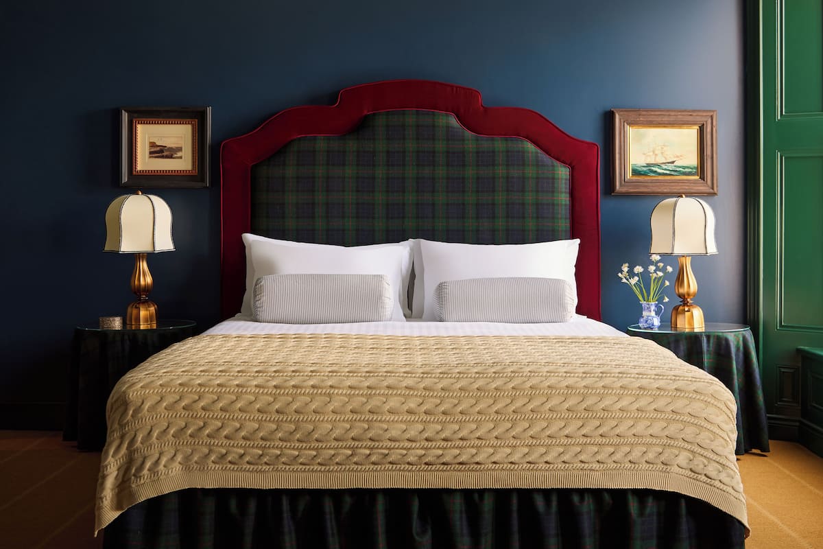 A bed with a plaid headboard, two bedside tables with lamps, and framed pictures on the walls.