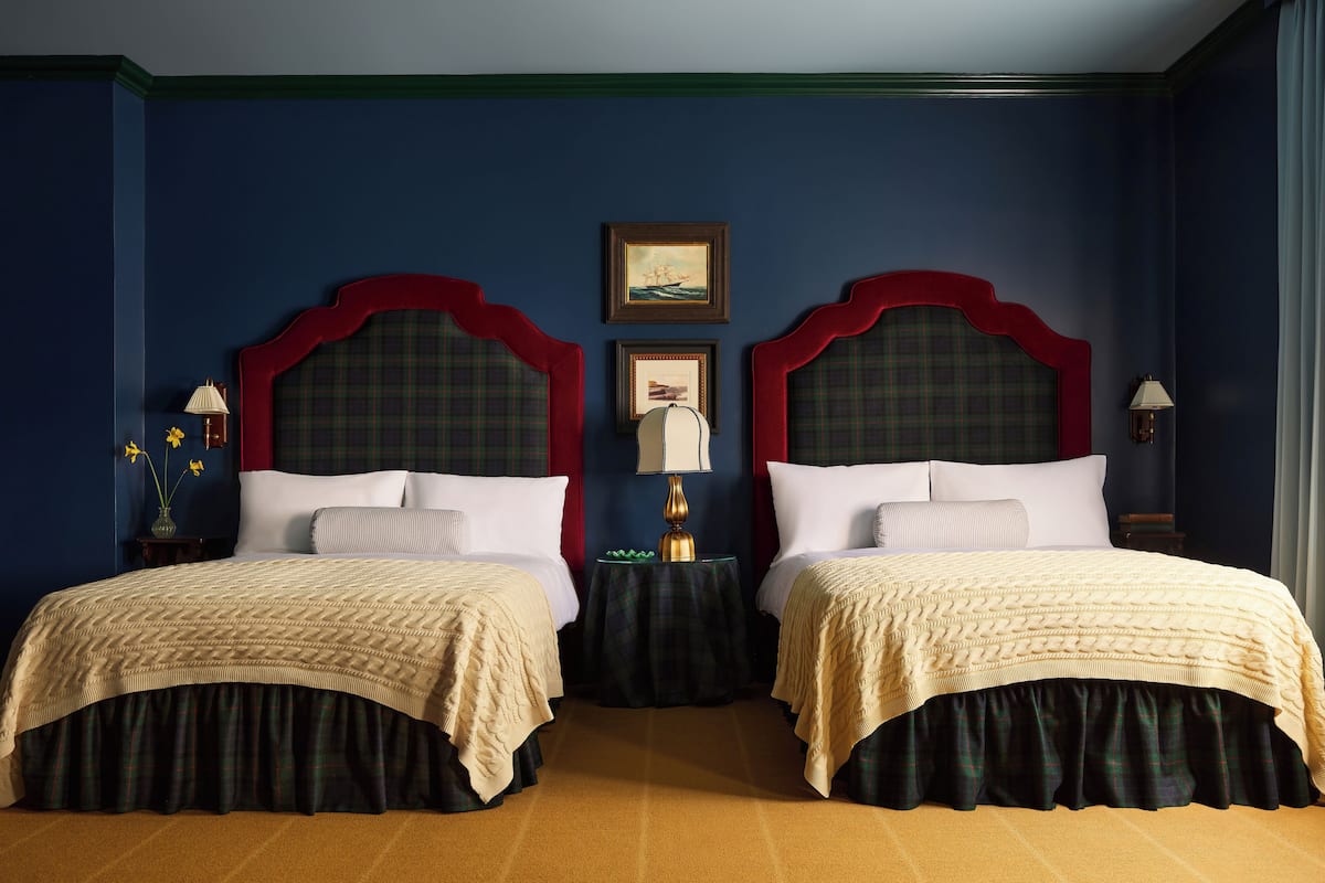 A double room with two beds, a small table, and a painting on the wall.