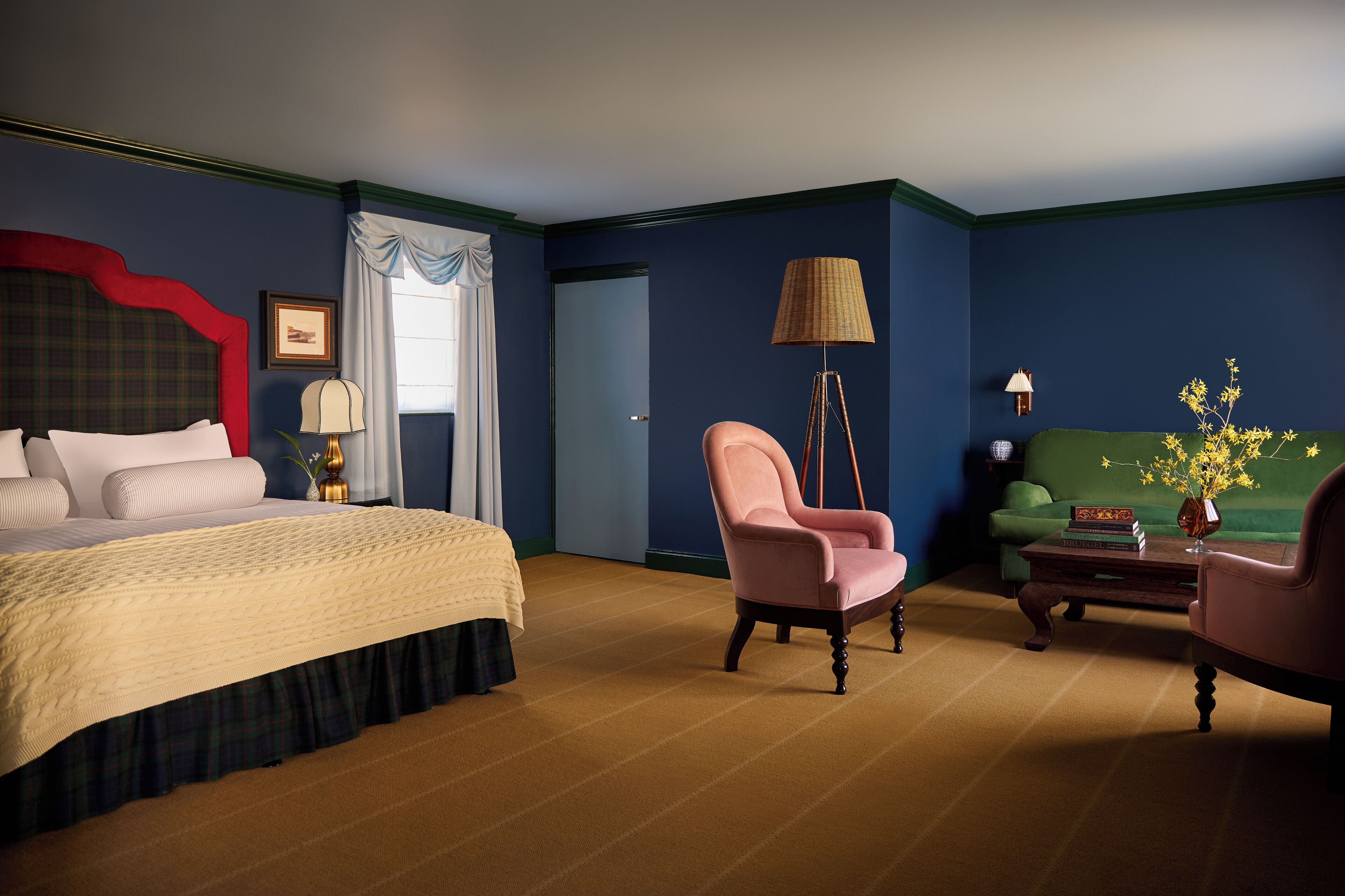 A hotel room with a bed, a chair, a lamp, a side table, and a green sofa.