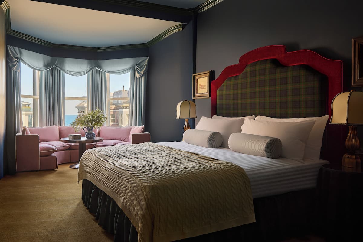 A hotel room with a large bed, a sofa, a small table, and a view of the city.