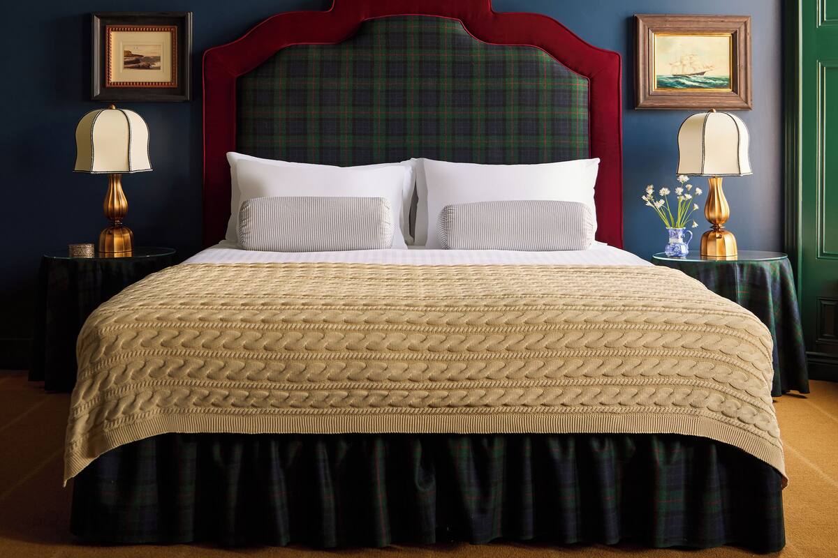 A bed with a plaid headboard, two bedside tables with lamps, and framed pictures on the walls.