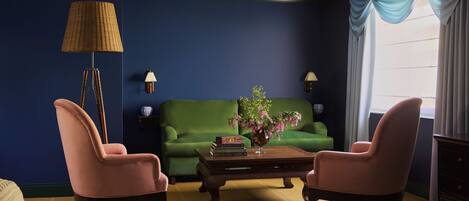 A room with a green sofa, two pink armchairs, a wooden coffee table, a floor lamp, and a window with curtains.