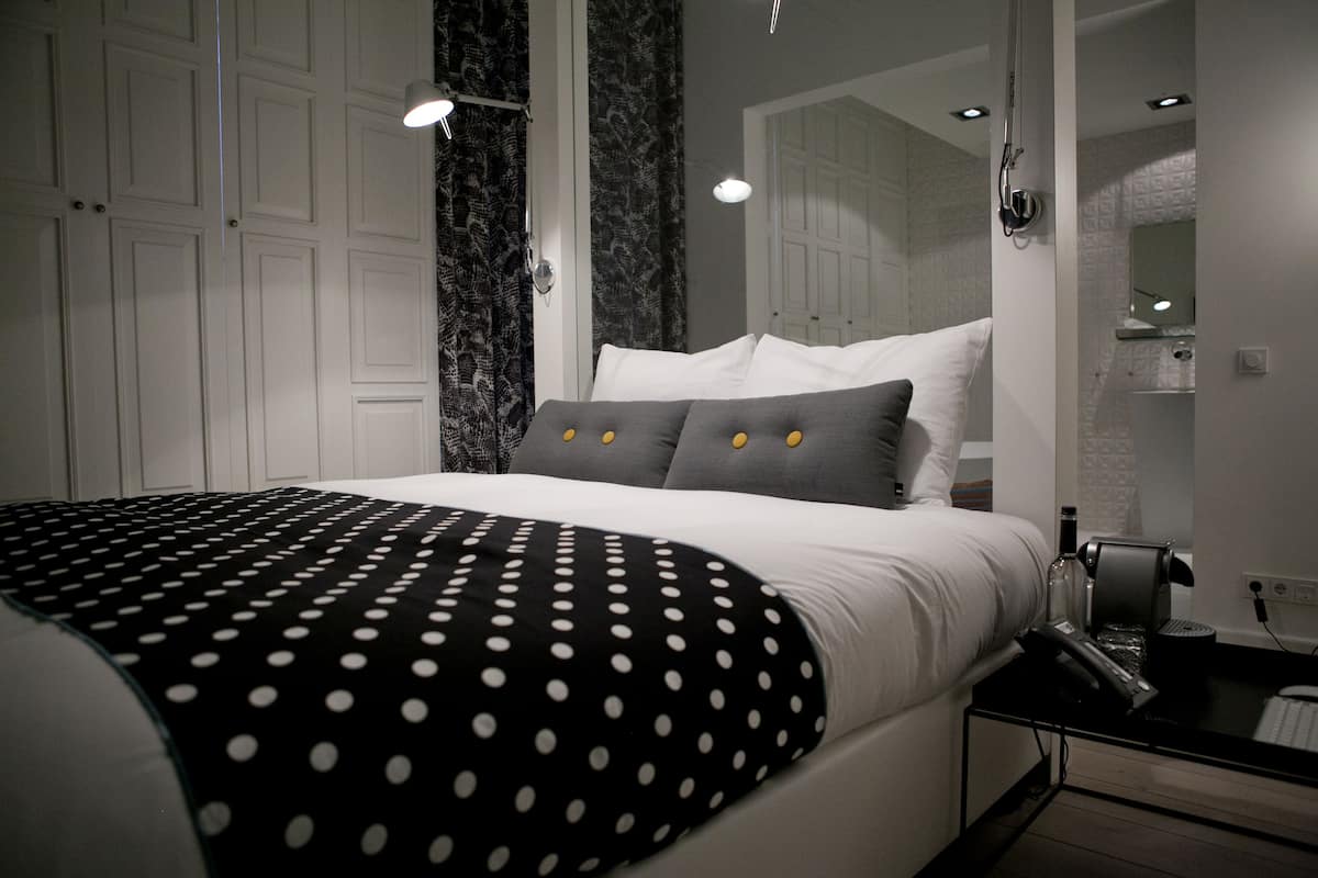 A modern bedroom with a bed, a nightstand, and a bathroom mirror.