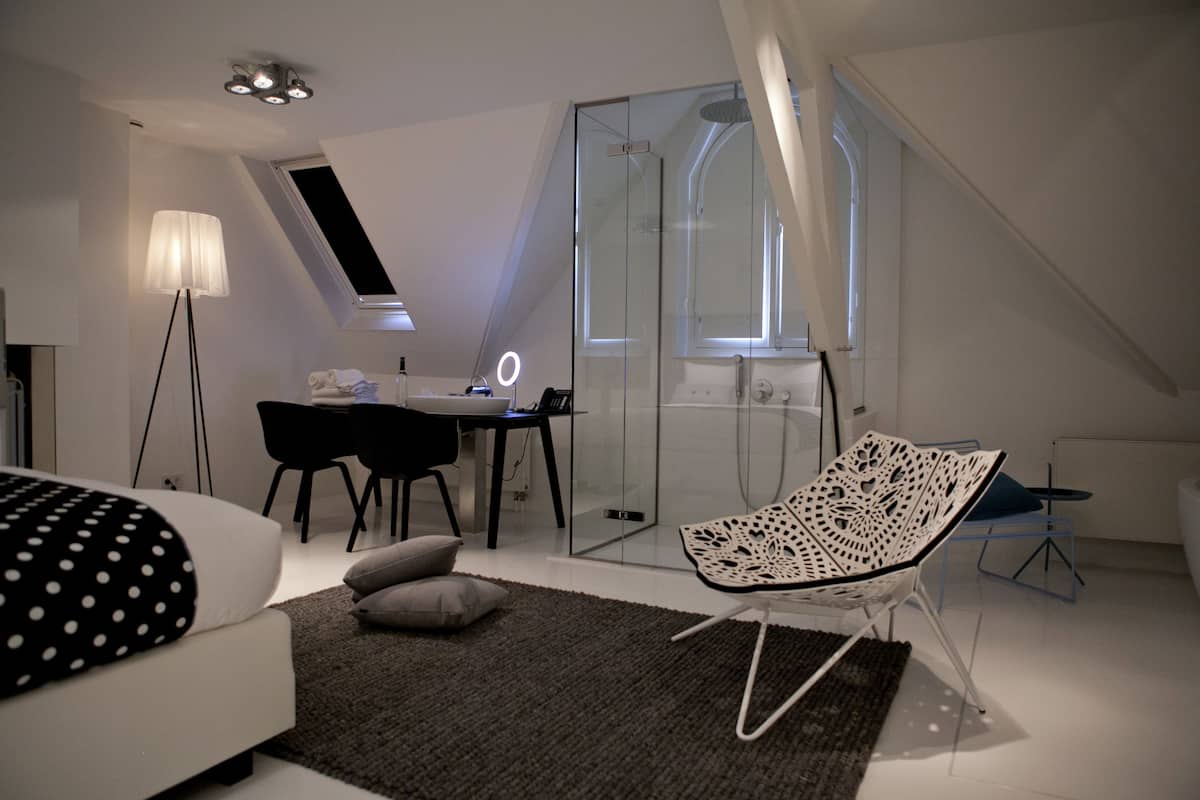 A modern bedroom with a bed, a desk, a chair, and a glass shower enclosure.