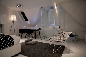 A modern bedroom with a bed, a desk, a chair, and a glass shower enclosure. - Boutique Hotel MANNA - Quality Lodgings (Nijmegen)