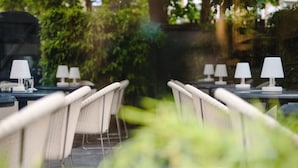 Una hilera de mesas al aire libre con sillas, cada una con una lámpara de mesa blanca.