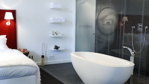 Un baño moderno con una bañera independiente, cabina de ducha y mesita de noche con artículos de aseo.