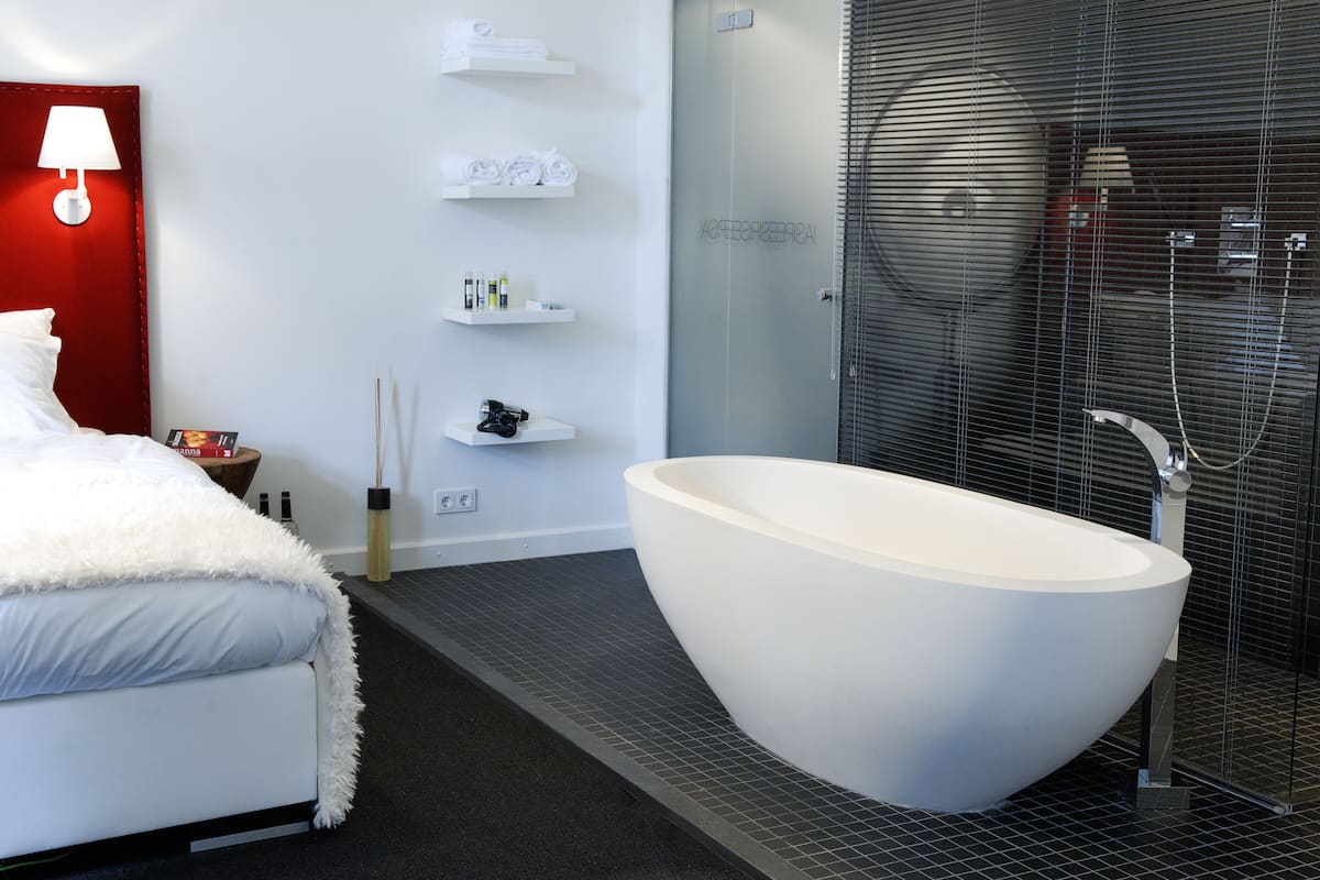 A modern bathroom with a freestanding bathtub, a shower enclosure, and a bedside table with toiletries.