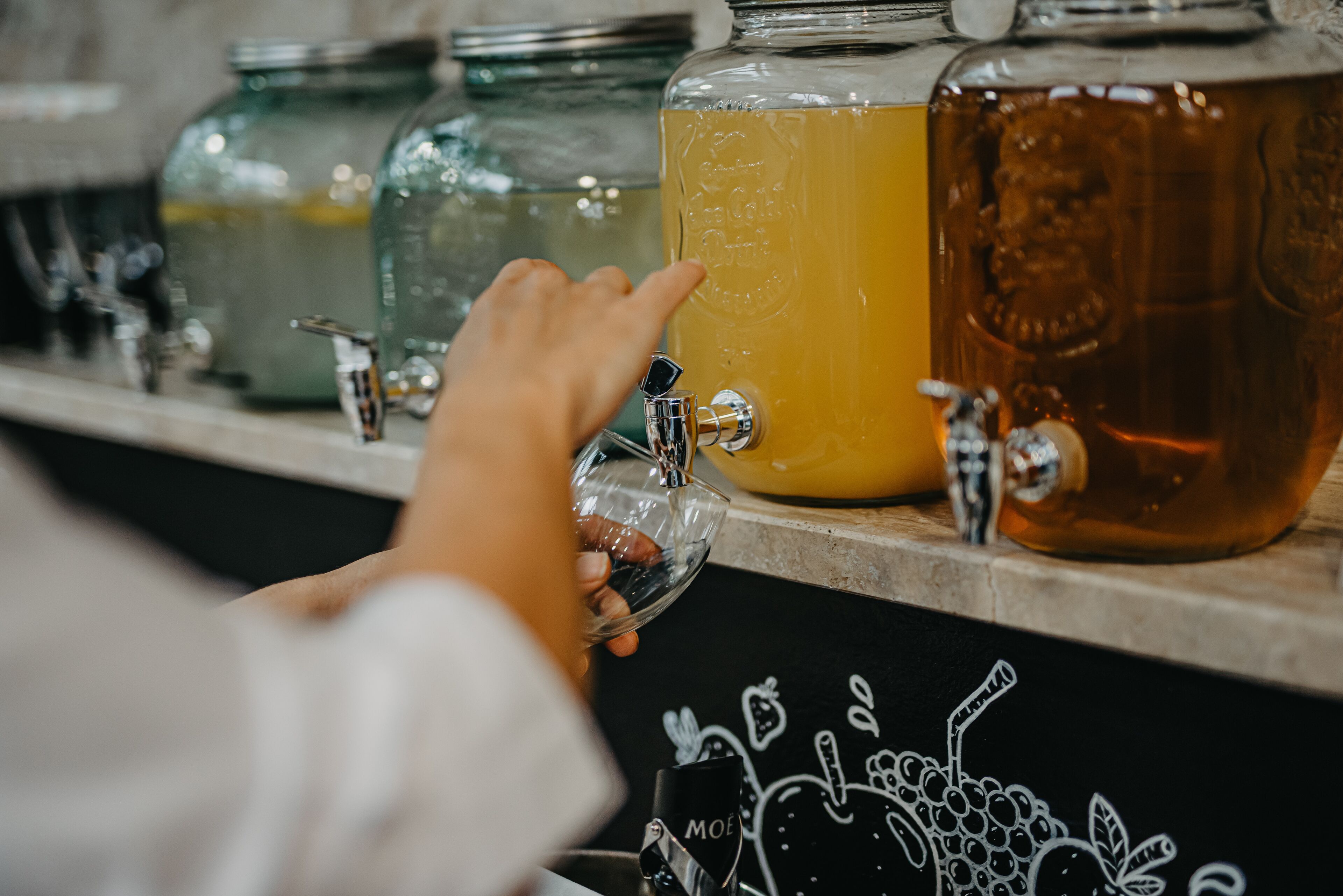 A hand reaching for a tap to fill a glass from a large container.