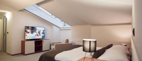 A modern hotel room with a skylight, a television, a bed, a desk, and a chair.