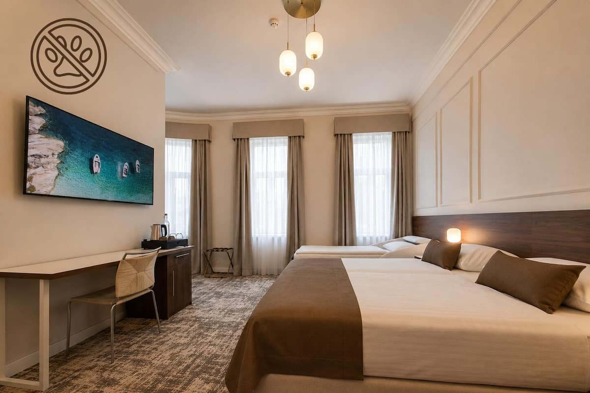 Habitación de hotel con cama, escritorio, silla y un cuadro de una escena costera.