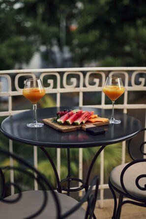 A table with two drinks and a fruit platter on a balcony with metal railings and greenery in the background. - Hotel Villa Eugenia (Lovran)