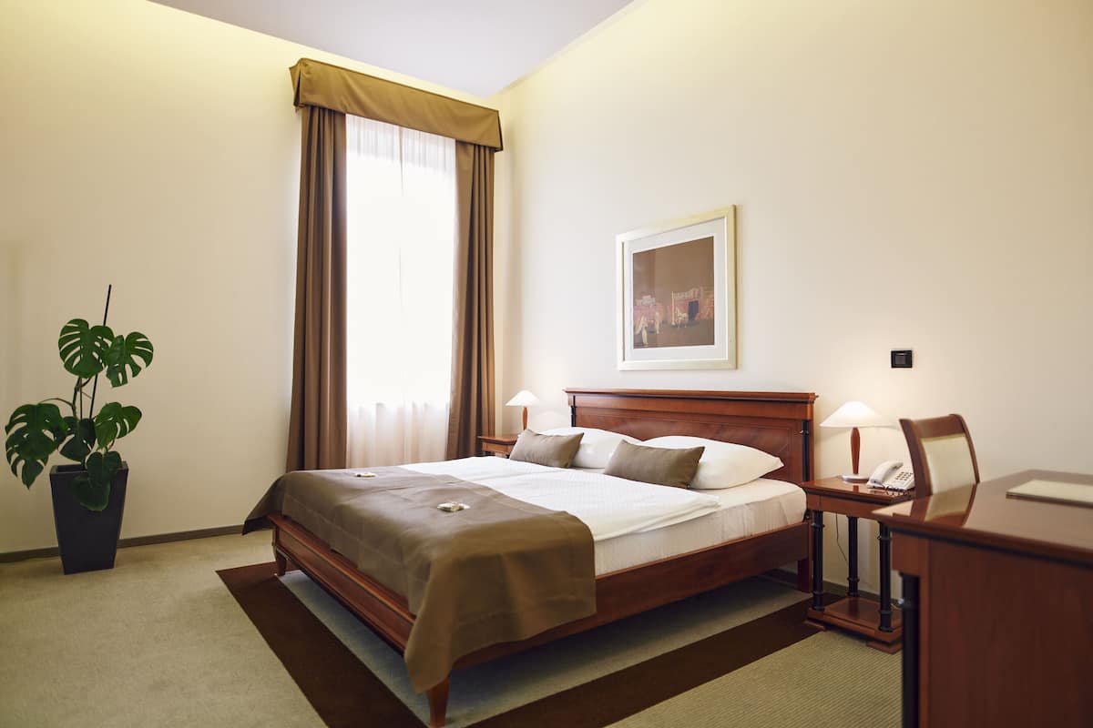 Habitación de hotel con cama, lámparas de noche, un escritorio, una silla, una planta en maceta y una ventana con cortinas.