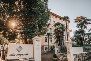 A building with a sign reading "villa eugenia" at the entrance, surrounded by palm trees and a stone wall. - Hotel Villa Eugenia (Lovran)