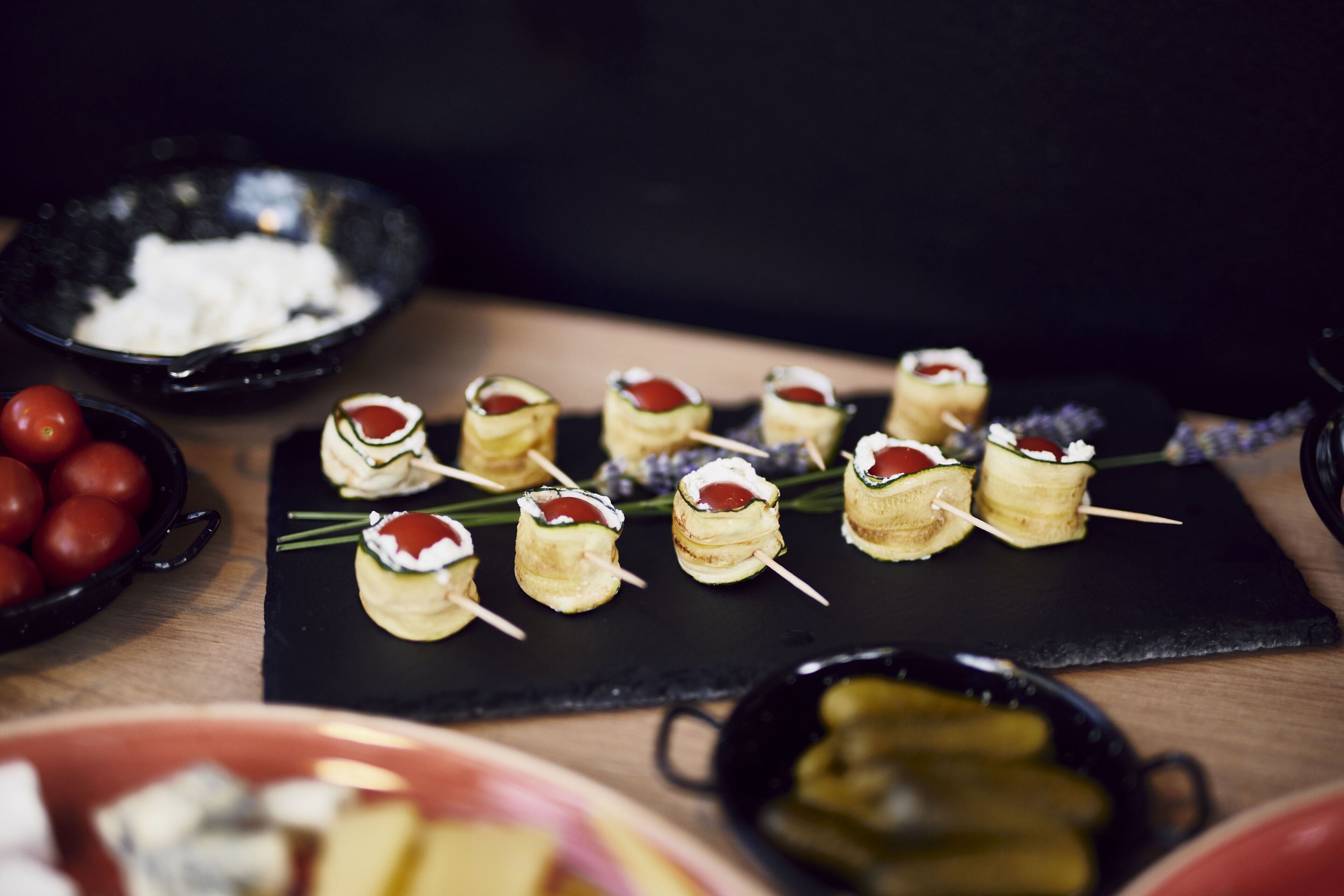 Verschiedene Speisen auf einer schwarzen Schiefertafel, darunter Spieße und eine Schale mit Cocktailtomaten.