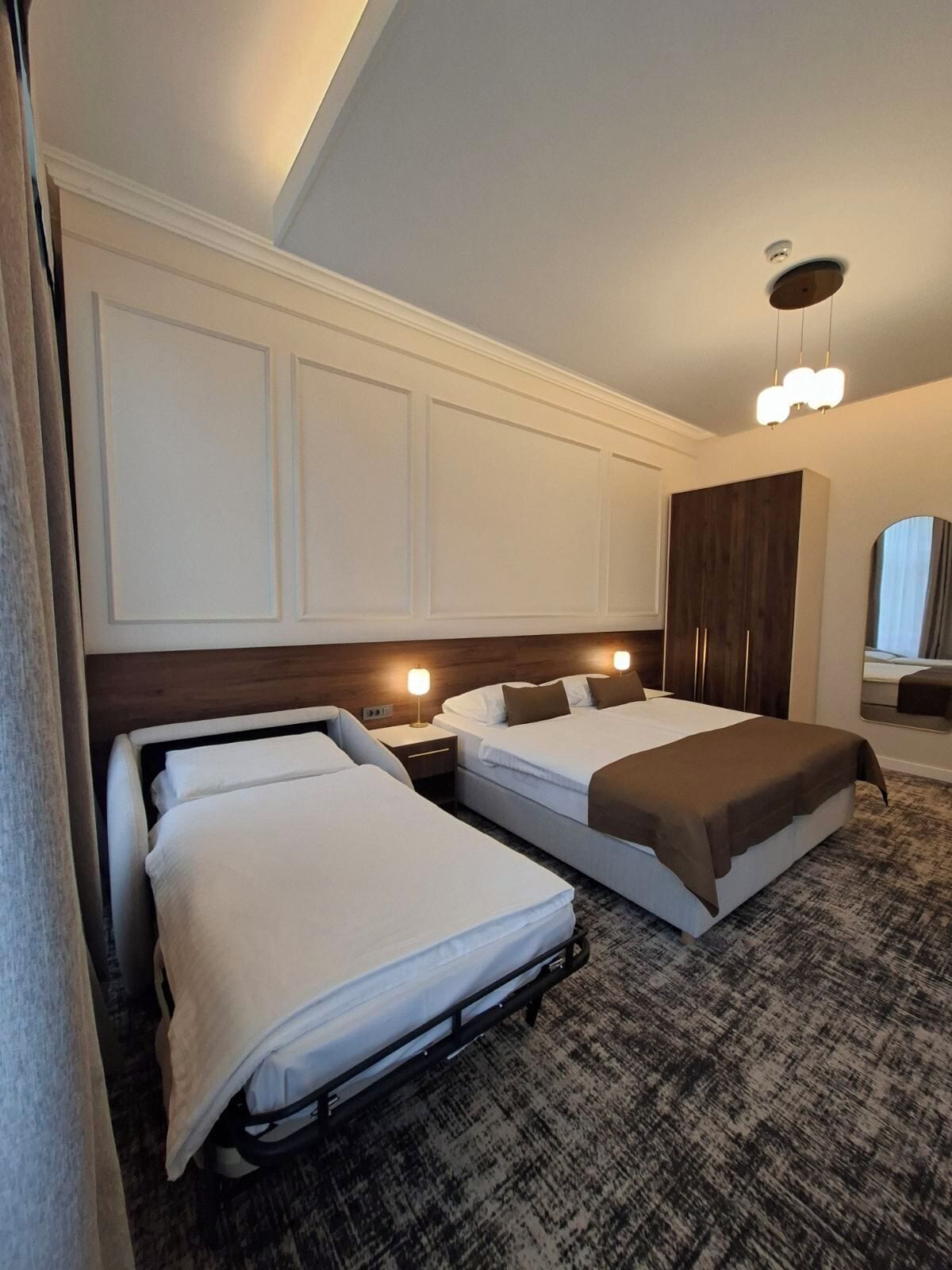 A hotel room with two beds, a wardrobe, a mirror, and a ceiling light fixture.
