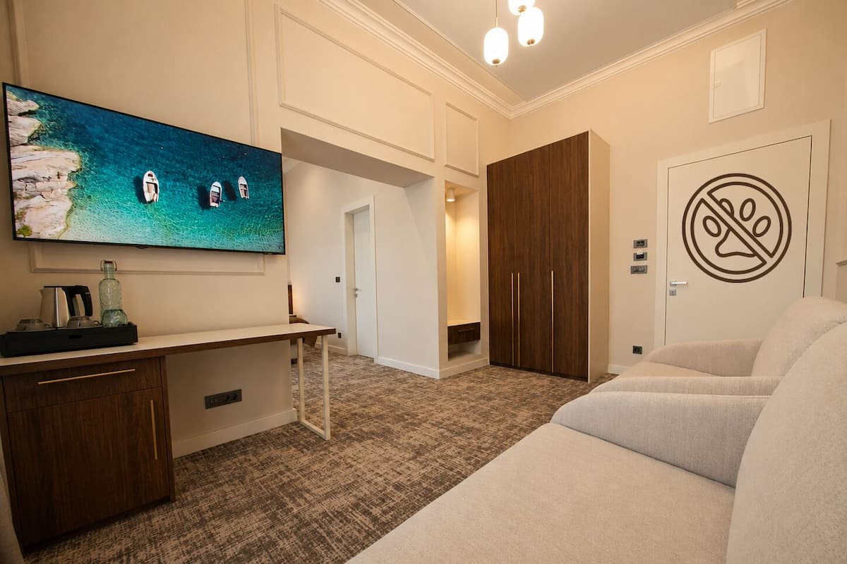 Habitación de hotel con televisor grande, escritorio, sofá, armario y puerta con cartel de prohibido fumar.