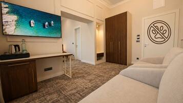 A hotel room with a large TV, a desk, a sofa, a wardrobe, and a door with a no-smoking sign.