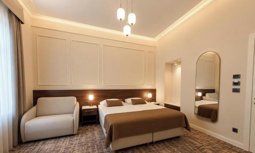 A hotel room with a bed, a chair, bedside tables, a mirror, and a carpeted floor.