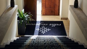 A wooden double door with glass panels, a black doormat with a floral design, and a potted plant to the left. - Hotel Villa Eugenia (Lovran)