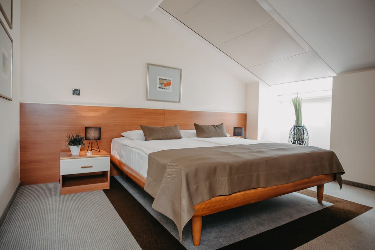Un dormitorio moderno con cabecera de madera, una cama grande, una mesita de noche con lámpara y un cuadro enmarcado en la pared.