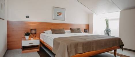 A modern bedroom with a wooden headboard, a large bed with a brown bedspread, a bedside table with a lamp, and a small potted plant.